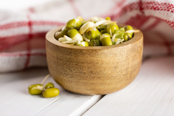 Lot of whole fresh green bean sprouts mungo with wooden bowl and a tea towel on white wood