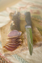 A dried ham on a wooden board cut into snacks with a knife next to it.