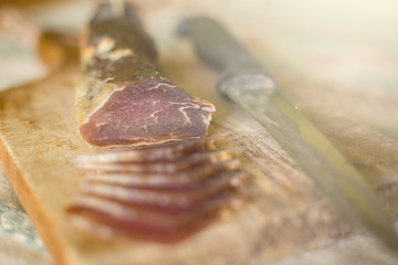 A dried ham on a wooden board cut into snacks with a knife next to it.