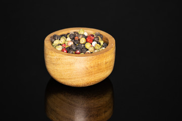 Lot of whole peppercorns of four colors with wooden bowl isolated on black glass