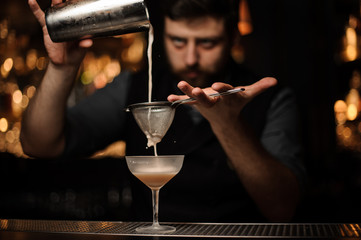 Brunette bartender pouring cocktail from the shaker through the strainer