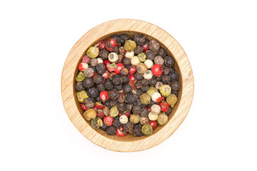 Lot of whole peppercorns of four colors with wooden bowl flatlay isolated on white background