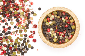 Lot of whole peppercorns of four colors with wooden bowl flatlay isolated on white background