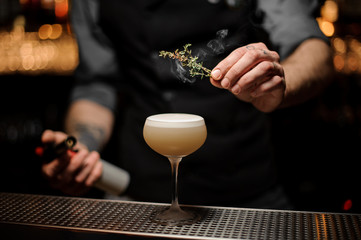 Bartender adding to a cocktail in the glass smoked herb
