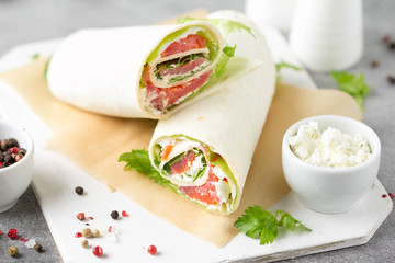 Tortilla with salmon, lettuce and cream cheese. Delicious snack wraps with fish and salad. Healthy burrito with pita bread for breakfast