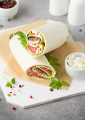 Tortilla with salmon, lettuce and cream cheese. Delicious snack wraps with fish and salad. Healthy burrito with pita bread for breakfast
