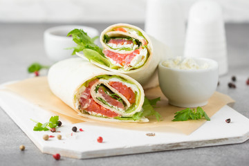 Tortilla with salmon, lettuce and cream cheese. Delicious snack wraps with fish and salad. Healthy burrito with pita bread for breakfast