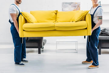 cropped view of two movers in uniform transporting couch in apartment