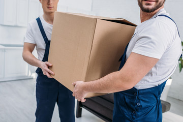 partial view of two movers transporting cardboard box in apartment