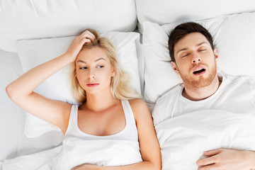 sleeping problems and people concept - unhappy woman lying in bed with snoring man