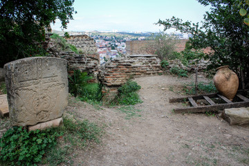 Church yard, tombstone, stone, jug, stairs. ruined stone wall. Religion. Summer, green plants, bushes. Georgia, Tbilisi, Narikala fortress.
