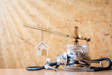 Use a stethoscope check a coin in the jar bank with growing value and tower crane  with build new house in the office, Saving money and loan for construction real estate and home concept.