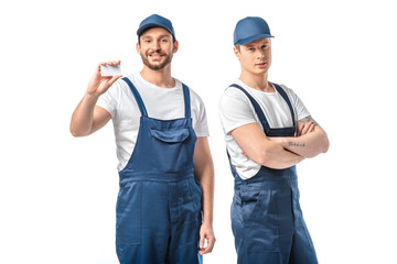 two movers in uniform looking at camera and showing empty business card isolated on white