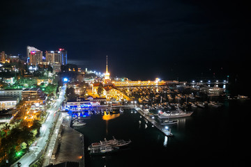Obraz na płótnie Canvas Sochi sea port. Aerial drone. Berth for marine yachts and boats. The historic building of the seaport. Evening illumination of the city.