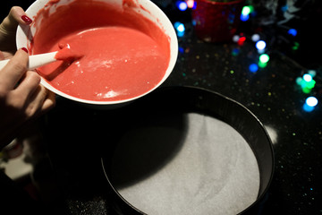 Woman is cooking in kitchen, baking a red velvet cake. Filling a biscuit tray with raw, uncooked dough. Delicious, homemade dessert