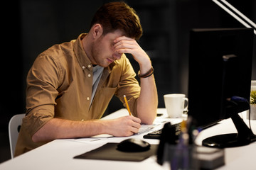 business, deadline and people concept - man with notepad and computer working late at night office