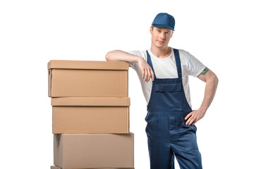 handsome mover in uniform with cardboard boxes looking at camera isolated on white