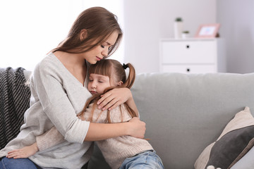 Sad woman after divorce hugging her little daughter while sitting on sofa