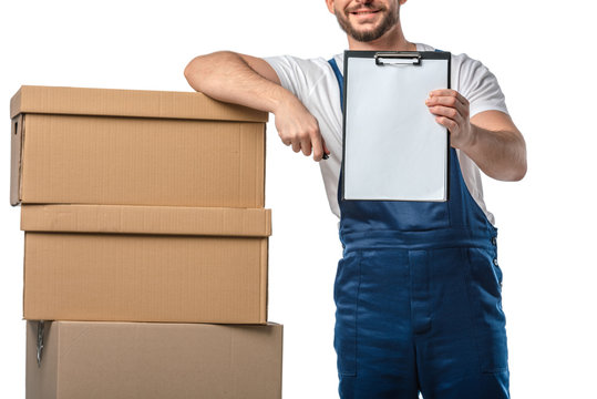 cropped view of mover in uniform holding blank clipboard near cardboard boxes isolated on white