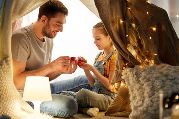 family, hygge and people concept - happy father and little daughter playing tea party in kids tent...