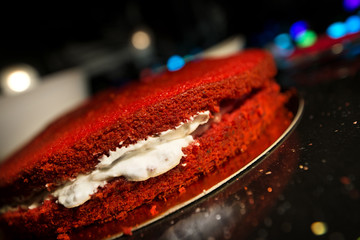Woman spreading whipped cream with fingers inside freshly made cake. Beautiful home made red velvet cake decorated with whipped cream and raspberry crumbs. Concept of anti sanitary cooking 