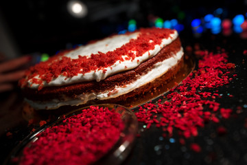 Woman sprinkling raspberry crumbs, icing sugar over freshly made cake, creating ornaments and decorating dessert. Beautiful home made red velvet cake decorated with whipped cream and raspberry crumbs