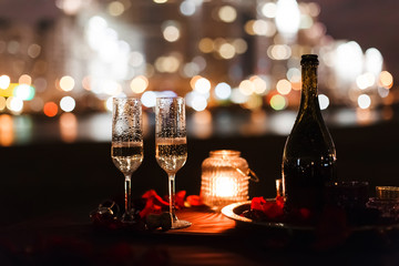 Romantic luxury evening with champagne setting with two glasses. rose petails and candles. Champagne for romantic celebrations or New Year party and enjoy for special moments. Bokeh background.