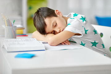 education, childhood and school concept - tired student boy sleeping on table at home