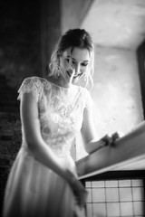 Model posing in a white long wedding dress indoors by the window. Advertising of wedding dresses