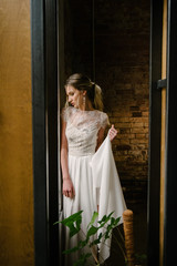 Model posing in a white long wedding dress indoors by the window. Advertising of wedding dresses