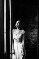 Model posing in a white long wedding dress indoors by the window. Advertising of wedding dresses