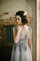 Fototapeta premium Model posing in a white long wedding dress indoors by the window. Advertising of wedding dresses