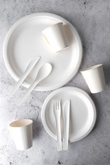 set of empty reusable disposable eco-friendly plates, cups, utensils on light white and grey concrete table top with copy space. Top view. 