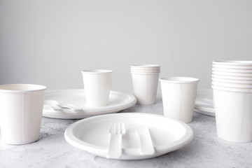 set of empty reusable disposable eco-friendly plates, cups, utensils on light white and grey...