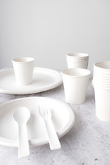 Fototapeta na wymiar set of empty reusable disposable eco-friendly plates, cups, utensils on light white and grey concrete table top on white wall blurred background with copy space. Top view. 
