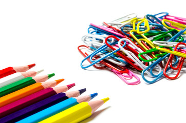 Many multi-colored stationery clips for documents and multi-colored pencils lie on a white background
