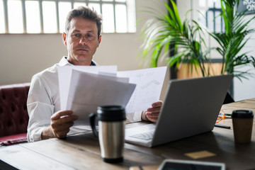 Focused businessman using laptop and reviewing documents at desk
