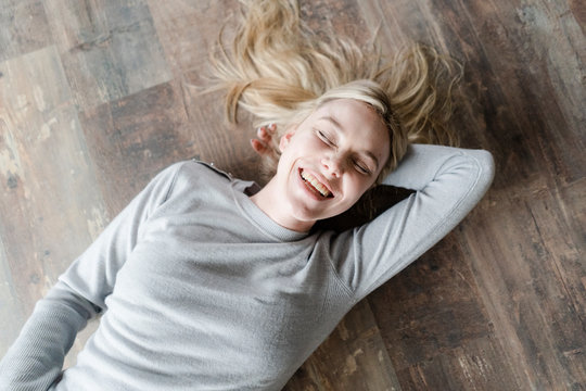 Happy blond young woman lying on wooden floor