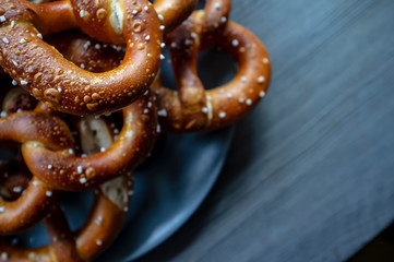 Appetizing, baked, soft pretzels with the addition of coarse salt in a plate, on a wooden textured table. Traditional food. Oktoberfest.