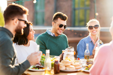 leisure and people concept - happy friends eating and drinking at rooftop party in summer