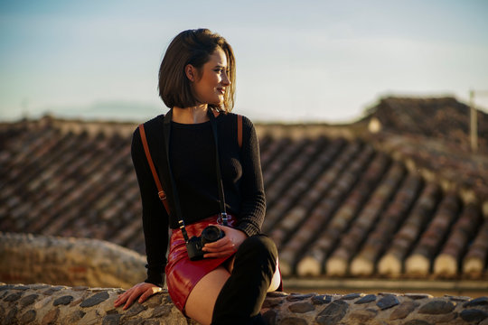 Young woman wearing red mini skirt sitting on a wall watching sunset