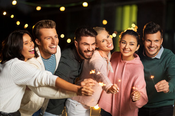 leisure, celebration and people concept - happy friends with sparklers at rooftop party at night