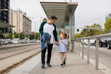 Smiling father and son walking hand in hand at tram stop in the city