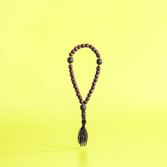 Wooden rosary levitating on a yellow background. Minimal concept.
