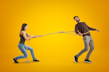 Side view of young woman lassooing young man on yellow background.