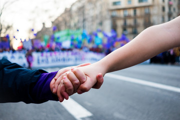 young women holding hands during woman's day rally with purple balloons in background for women...