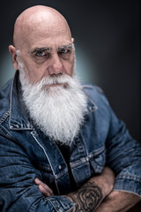studio portrait of a bald man with tattooed arms and white beard