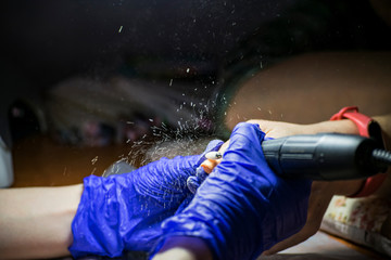 Manicurist removes old nail polish from nails with an electric machine.