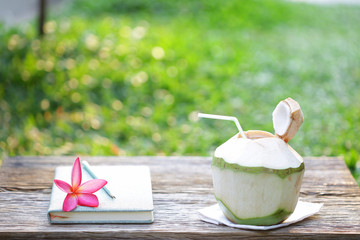 Coconut juice with pink frangipani on wooden table at outdoor in summer