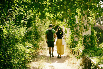 Fototapeta premium Young people go on a narrow alley. Wild grapes hang over the path. Selective focus. Blurred motion.